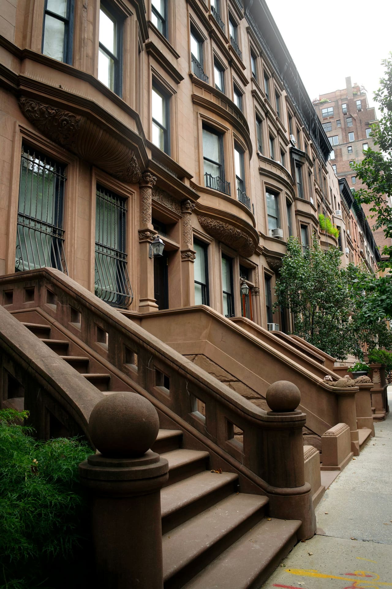 Row of brownstone townhouses with ornate stone stoops on a tree-lined Manhattan side street